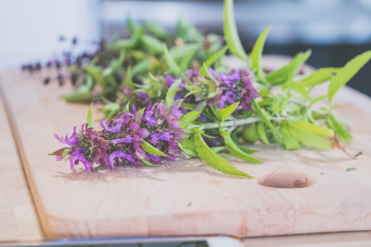 Close-up of purple flowers and herbs on a wooden board, ideal for natural therapy and herbal medicine themes.